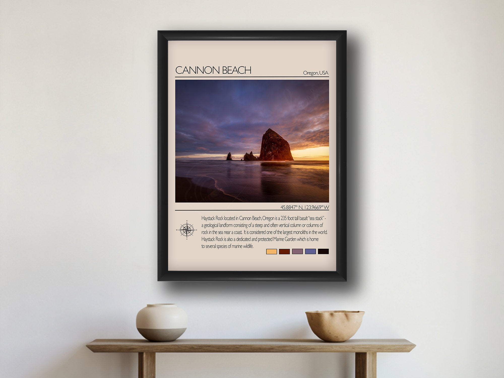 Canon Beach travel poster featuring Haystack Rock at sunset photograph and photo inspired color palette in black frame styled above a wooden table in a bright entryway